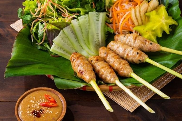 Những que nem lụi nướng vàng thơm, được cuốn trong bánh tráng cùng rau sống và chấm nước chấm đậu phộng.